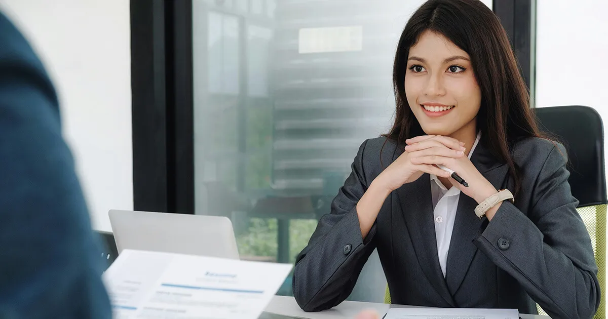 Two people in a formal German job interview across a table with a CV and notebook