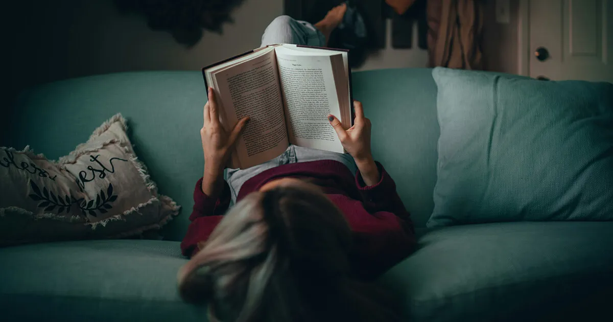Uma pessoa lendo relaxada um livro de bolso em idioma estrangeiro com um café